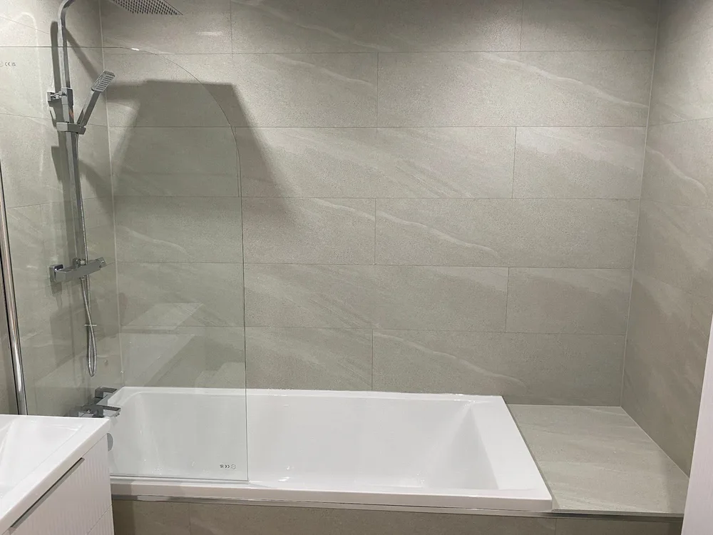 Bath with a shower screen and thermostatic mixer in a neutral tiled bathroom
