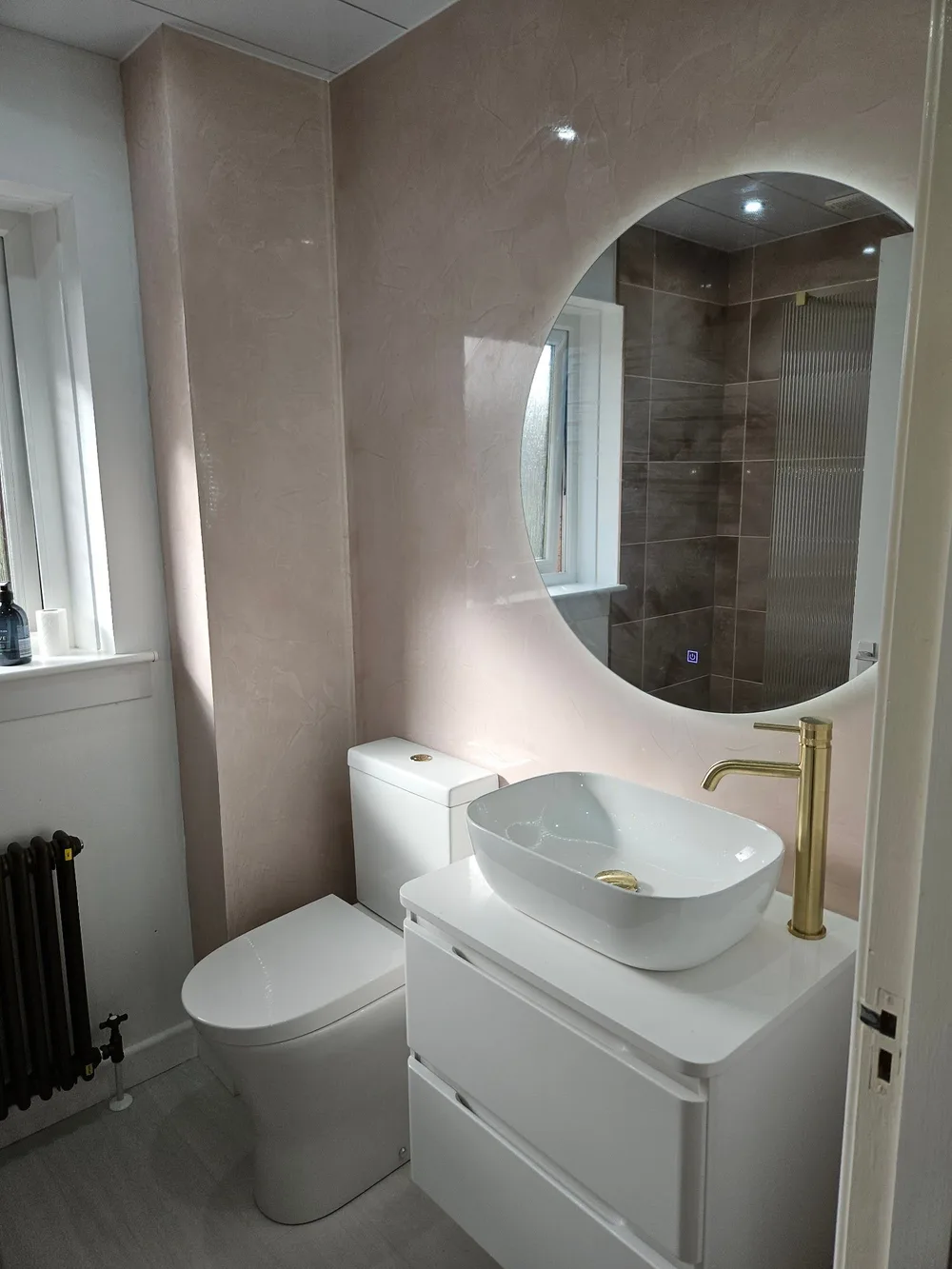 Cloakroom with a backlit round mirror, brushed brass tap and vessel basin