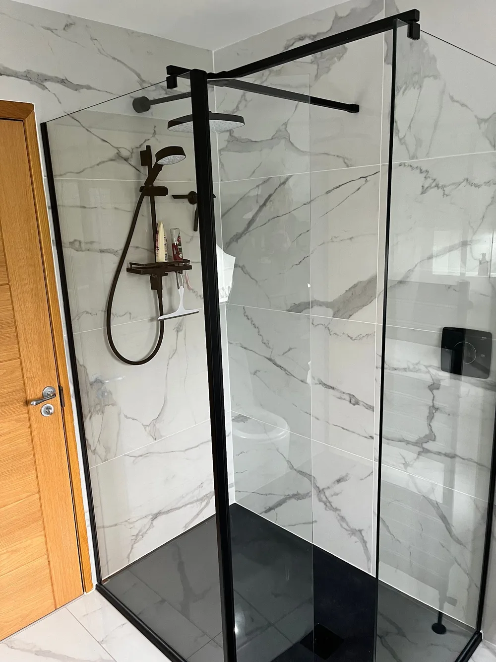 Walk-in shower with black framed glass against marble tiling